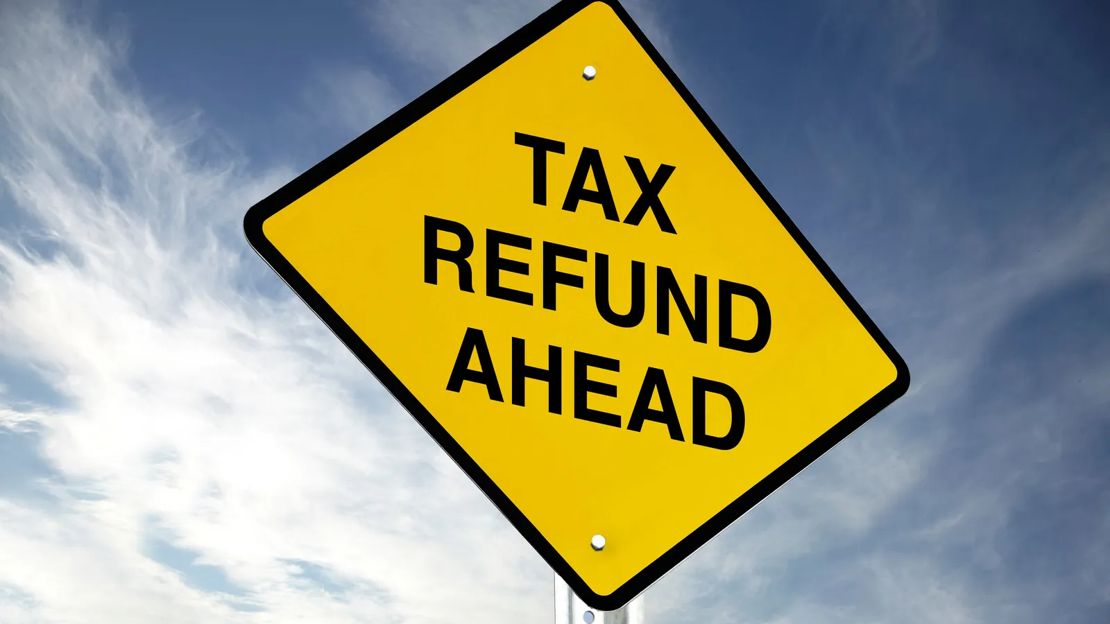Yellow diamond road sign with black border reading Tax Refund Ahead under a partly cloudy blue sky.