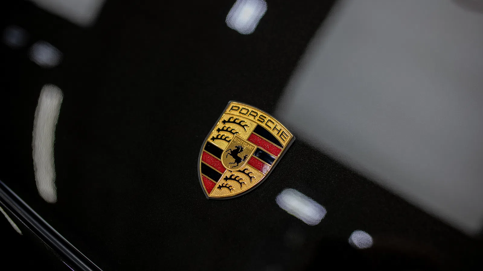 Close-up of the Porsche logo emblem on a glossy black car hood with reflections of light.