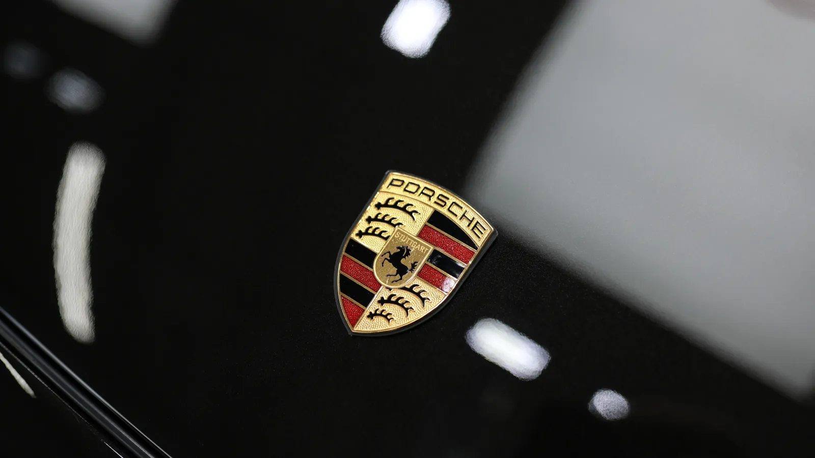 Close-up of the Porsche emblem on a glossy black car surface with reflections of light.