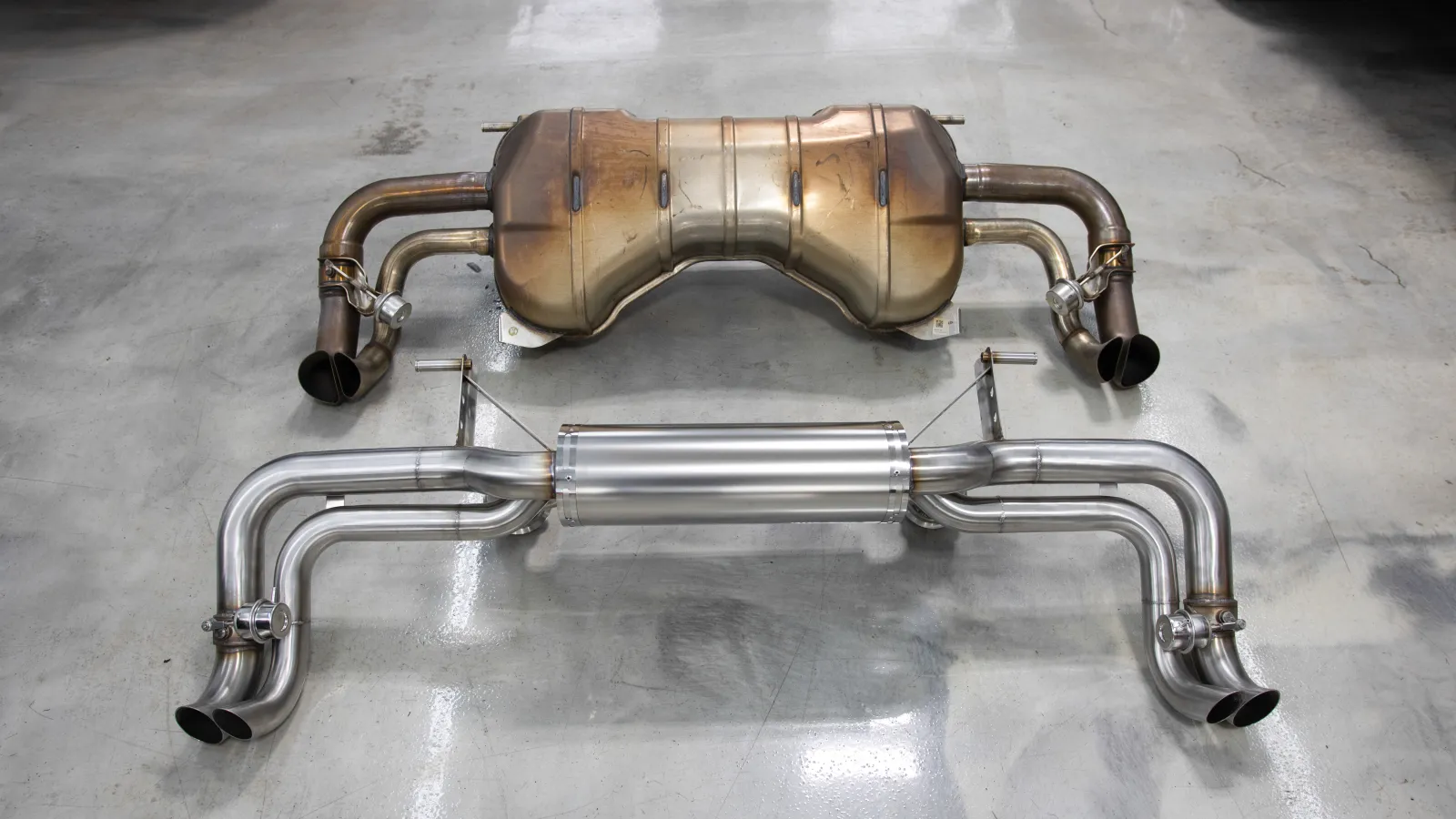 Comparison of old rusty and new shiny stainless steel car exhaust systems laid on concrete floor.