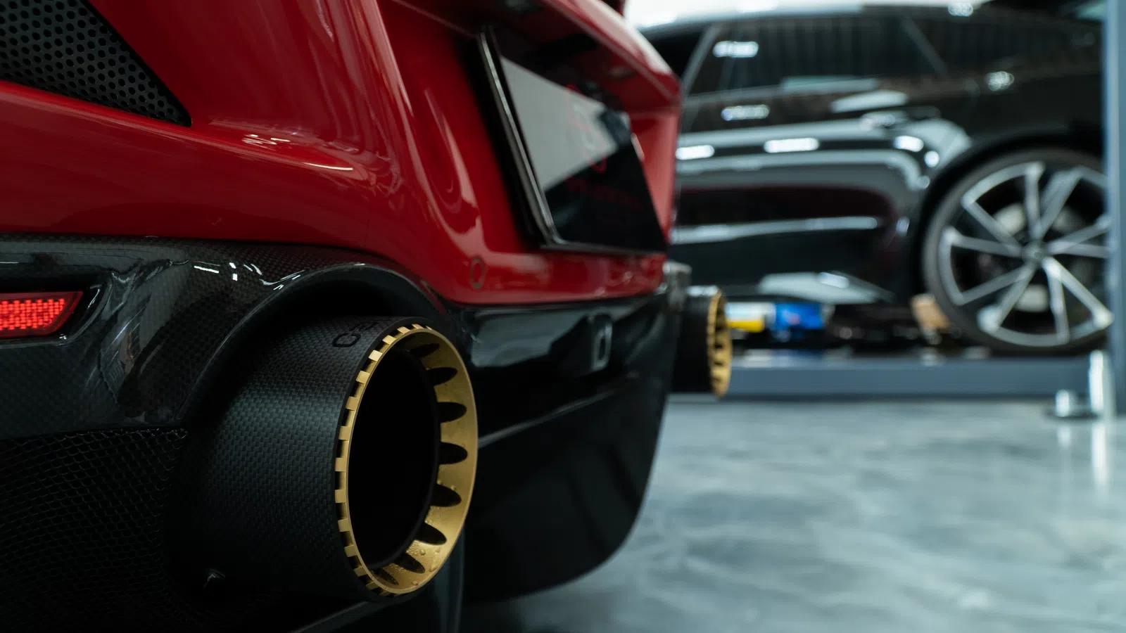 Close-up of a red sports car's dual carbon fiber exhaust tips with gold accents inside a garage.