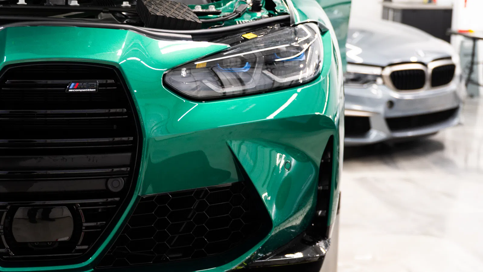 Close-up of front end of green BMW M car with distinctive grille and headlight design in showroom.