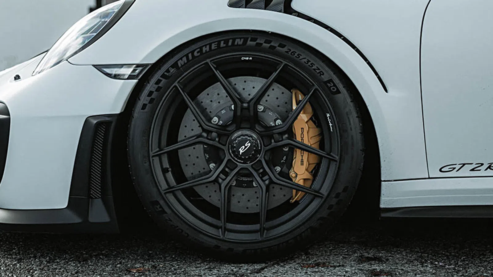 Close-up of a white Porsche GT2 RS front wheel with black alloy rim and yellow brake caliper on asphalt.