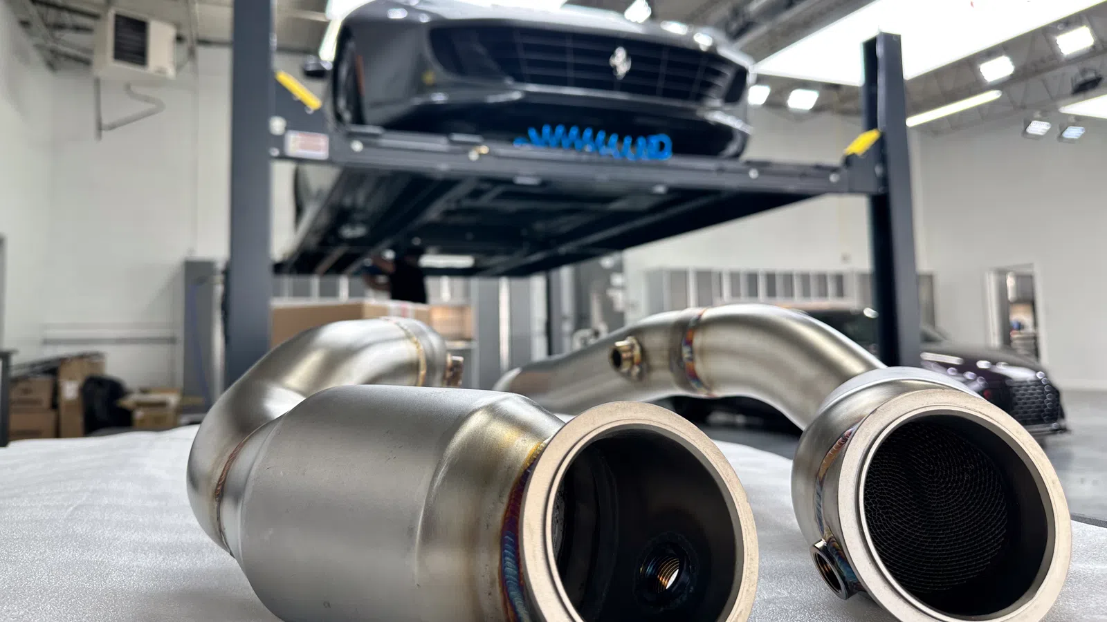 Close-up of stainless steel car exhaust pipes with a lifted Ferrari in a garage in the background