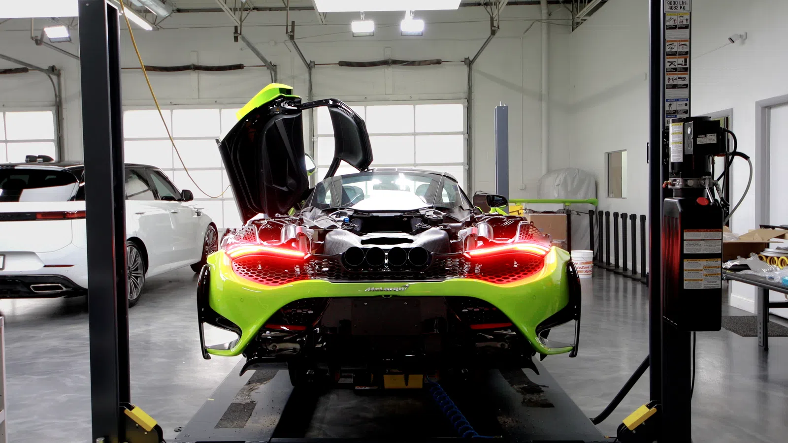 Bright green McLaren sports car with butterfly doors open inside a modern garage with another white car nearby