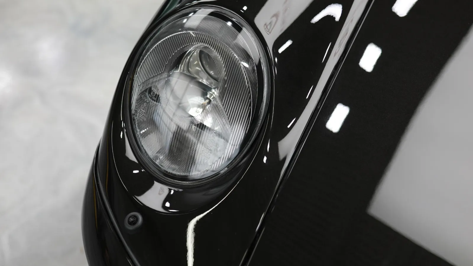 Close-up of a sleek black car's round headlight with reflective surface and smooth curves.