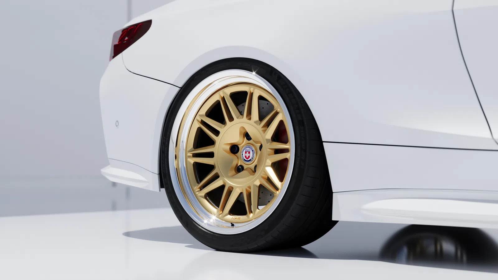 Close-up of a white car's rear with custom gold alloy wheel and low-profile tire on a clean background.
