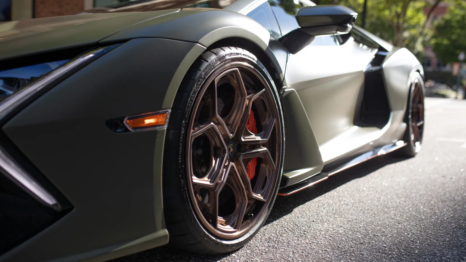 Close-up of matte green luxury sports car wheel and side, showcasing sleek design and high-performance brake calipers
