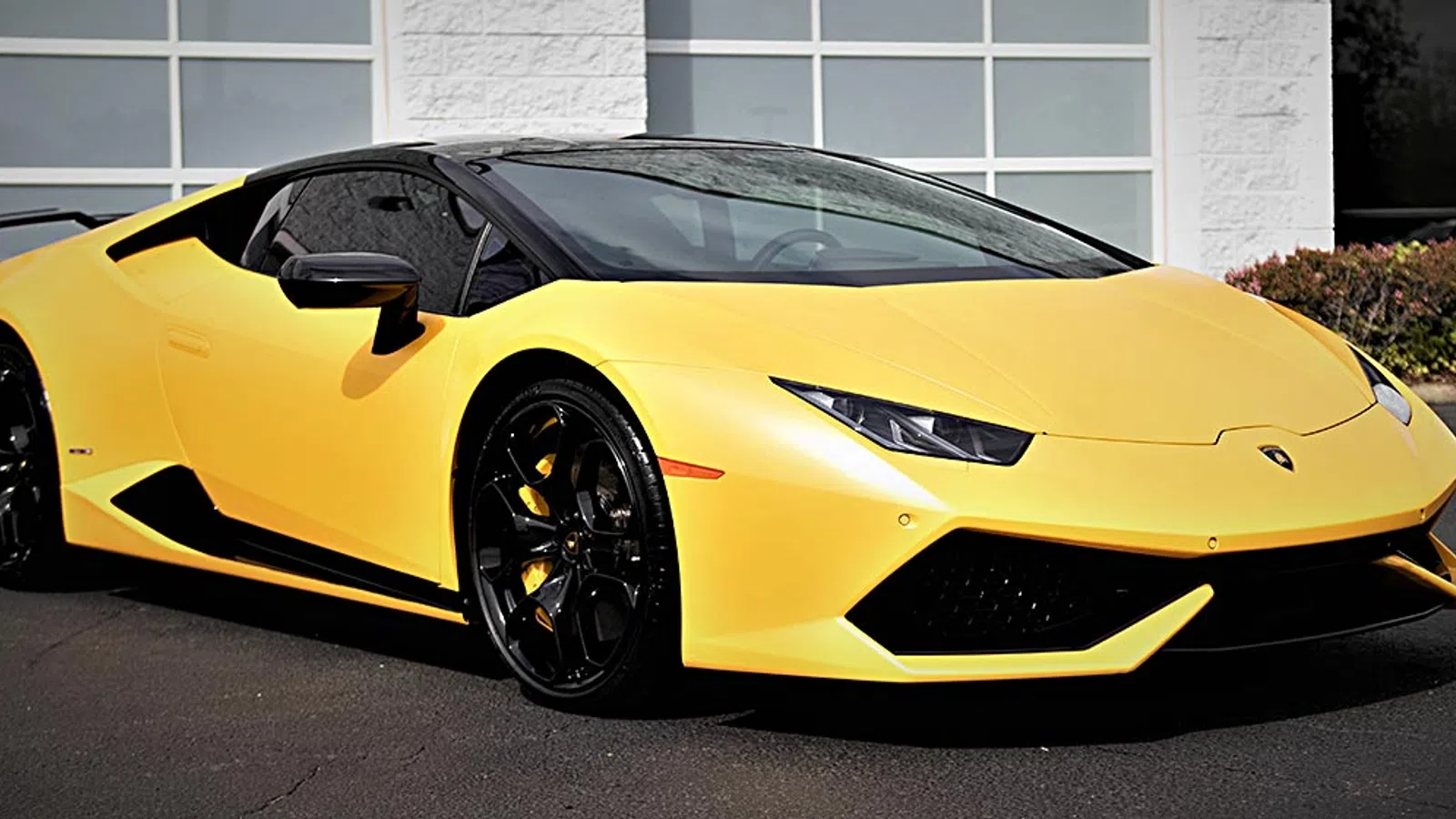 Yellow Lamborghini sports car parked outdoors in front of a white building with large windows.