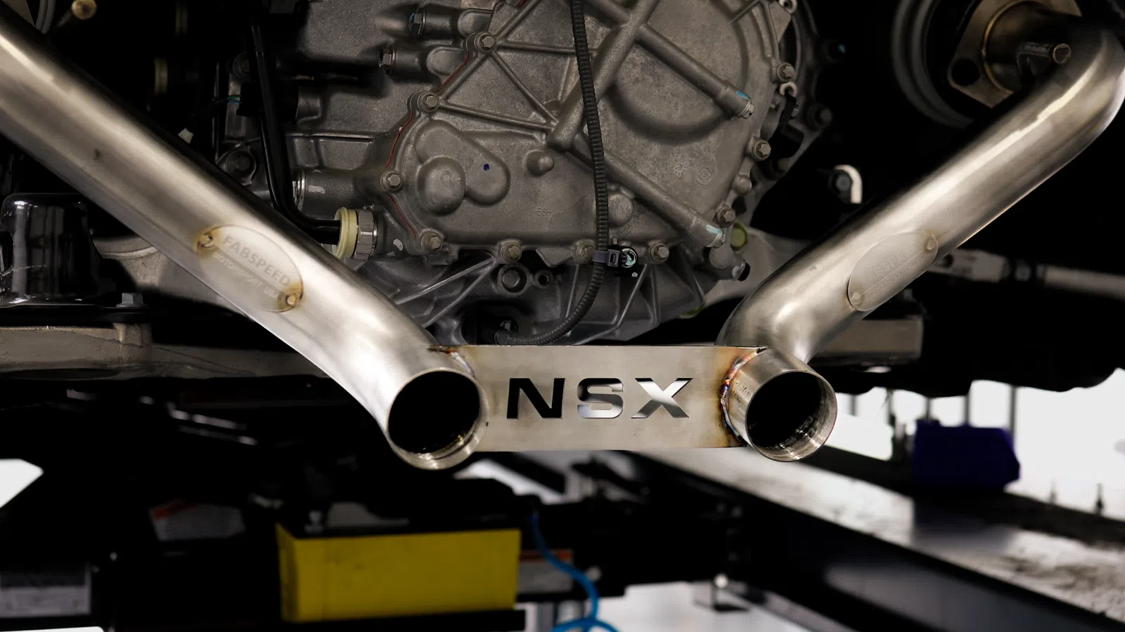 New stainless steel car exhaust system part displayed below an old rusty exhaust on a concrete floor.