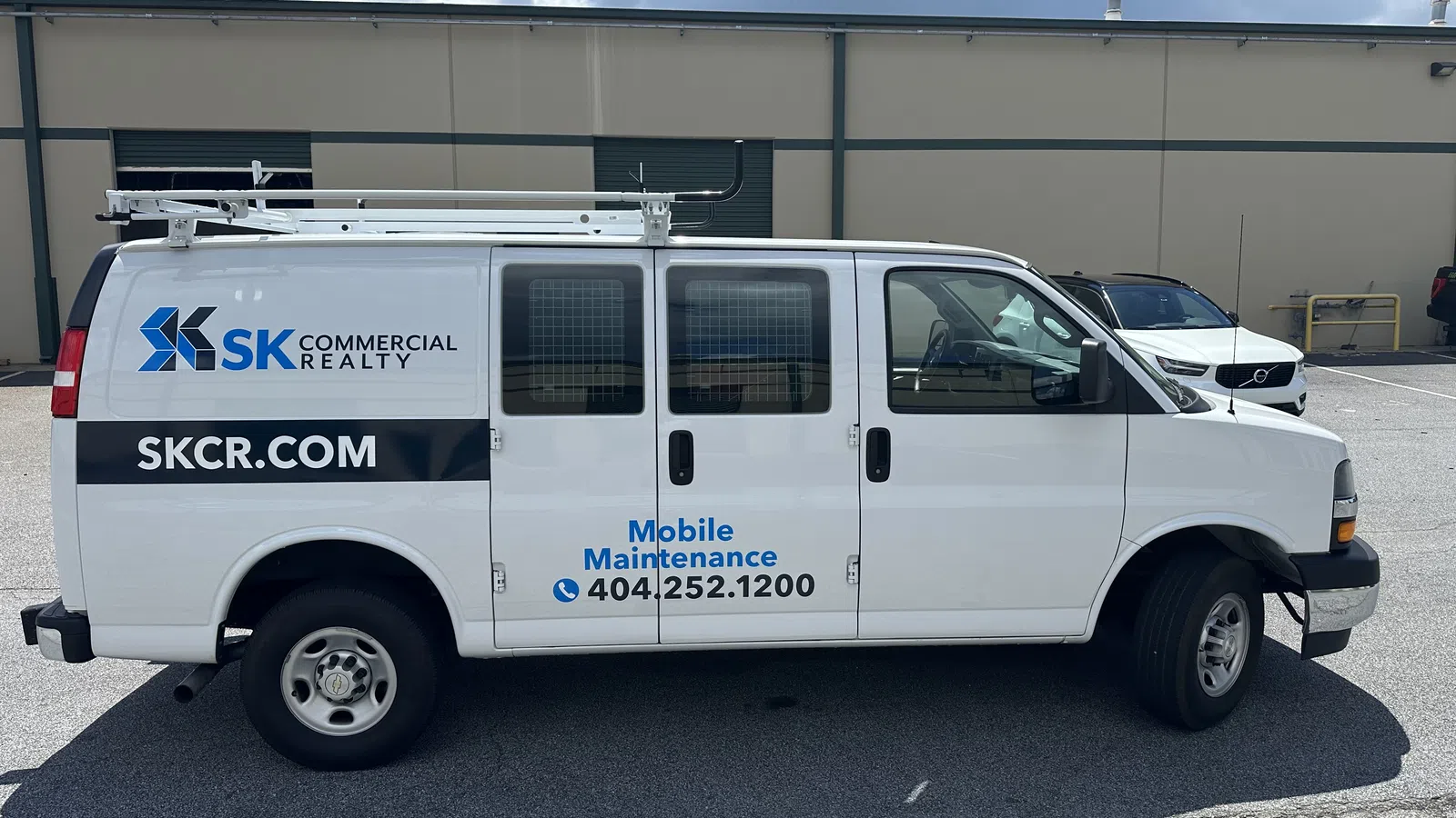 White mobile maintenance van with SK Commercial Realty branding and contact number parked outdoors on a sunny day.
