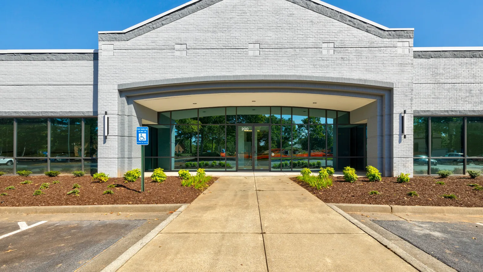Modern commercial building entrance with glass doors, landscaped garden, and blue sky in background