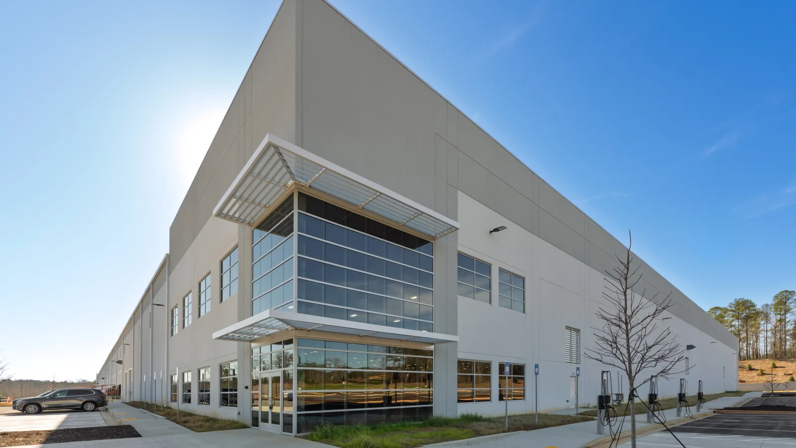 Large modern warehouse building with glass entrance under a clear blue sky and surrounding parking lot.