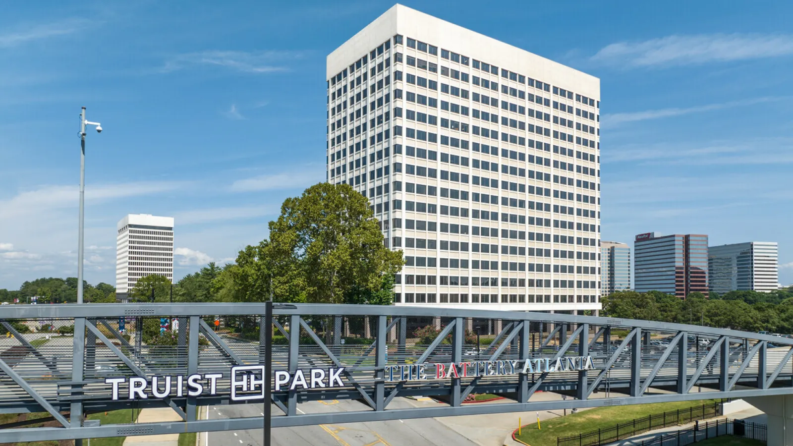Modern pedestrian bridge with Truist Park and The Battery Atlanta signs in front of tall office buildings under blue sky