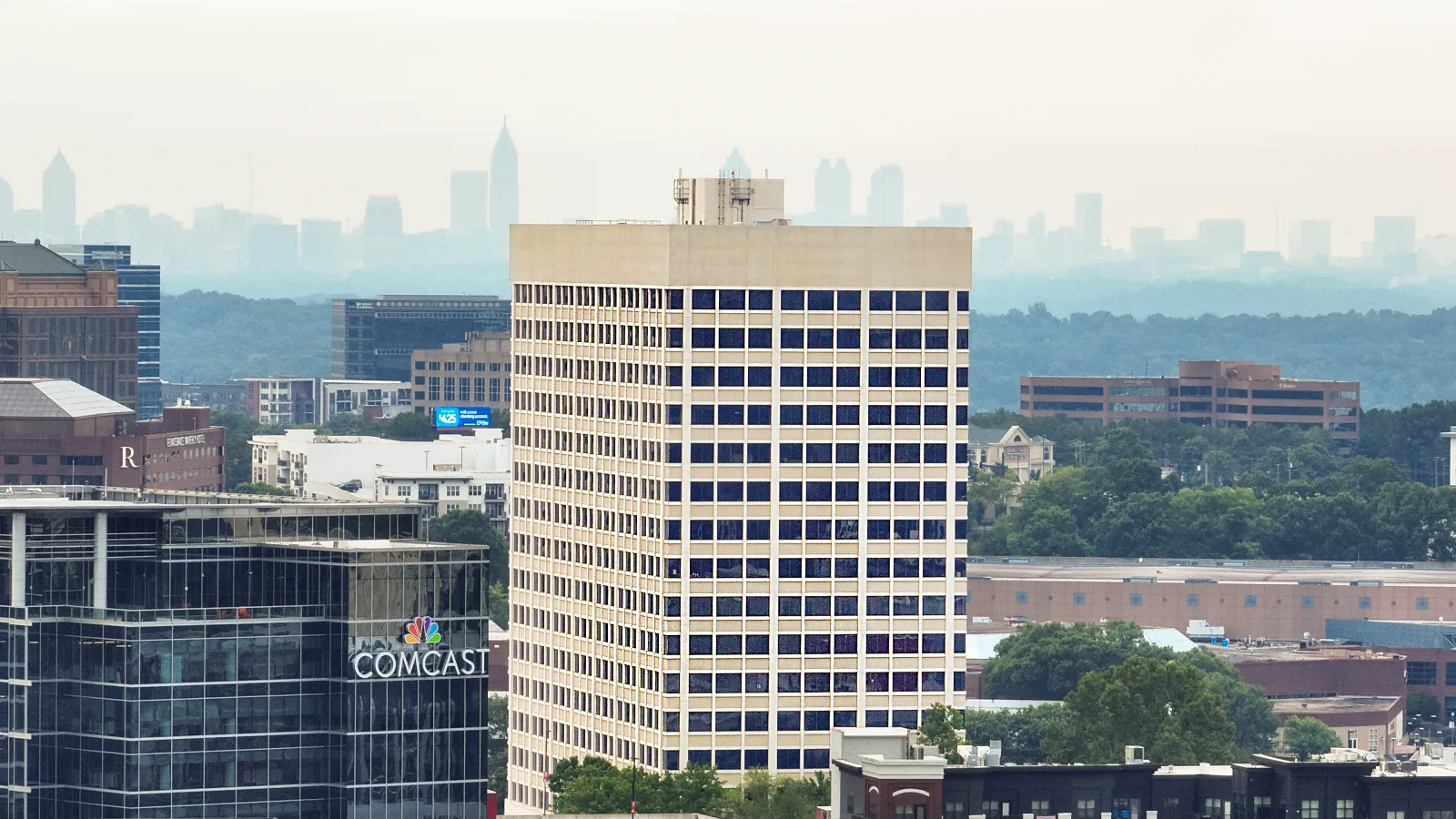View of urban buildings including Comcast Center with a hazy city skyline in the background under gray sky