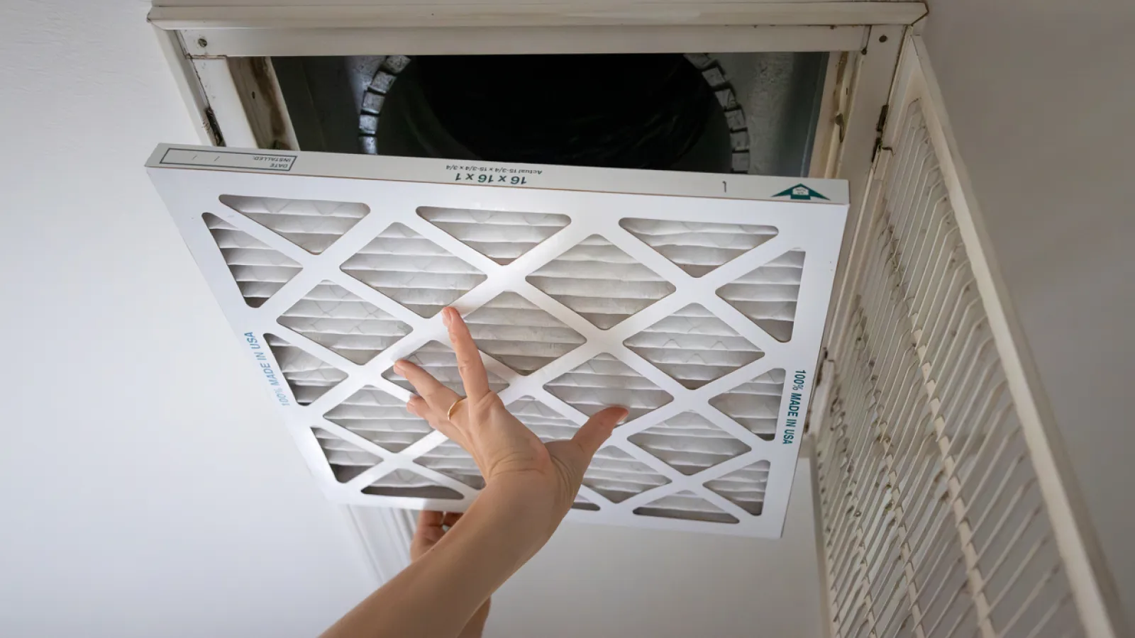 Person installing a white air filter into a ceiling air vent in a residential setting