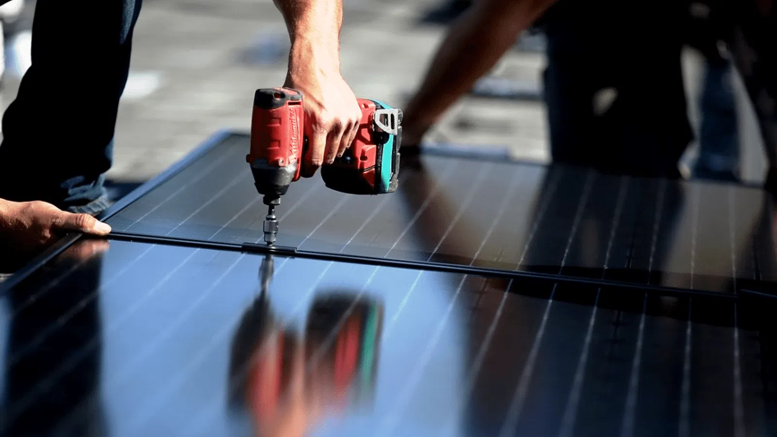Worker using a drill to install solar panels on a rooftop under sunny conditions