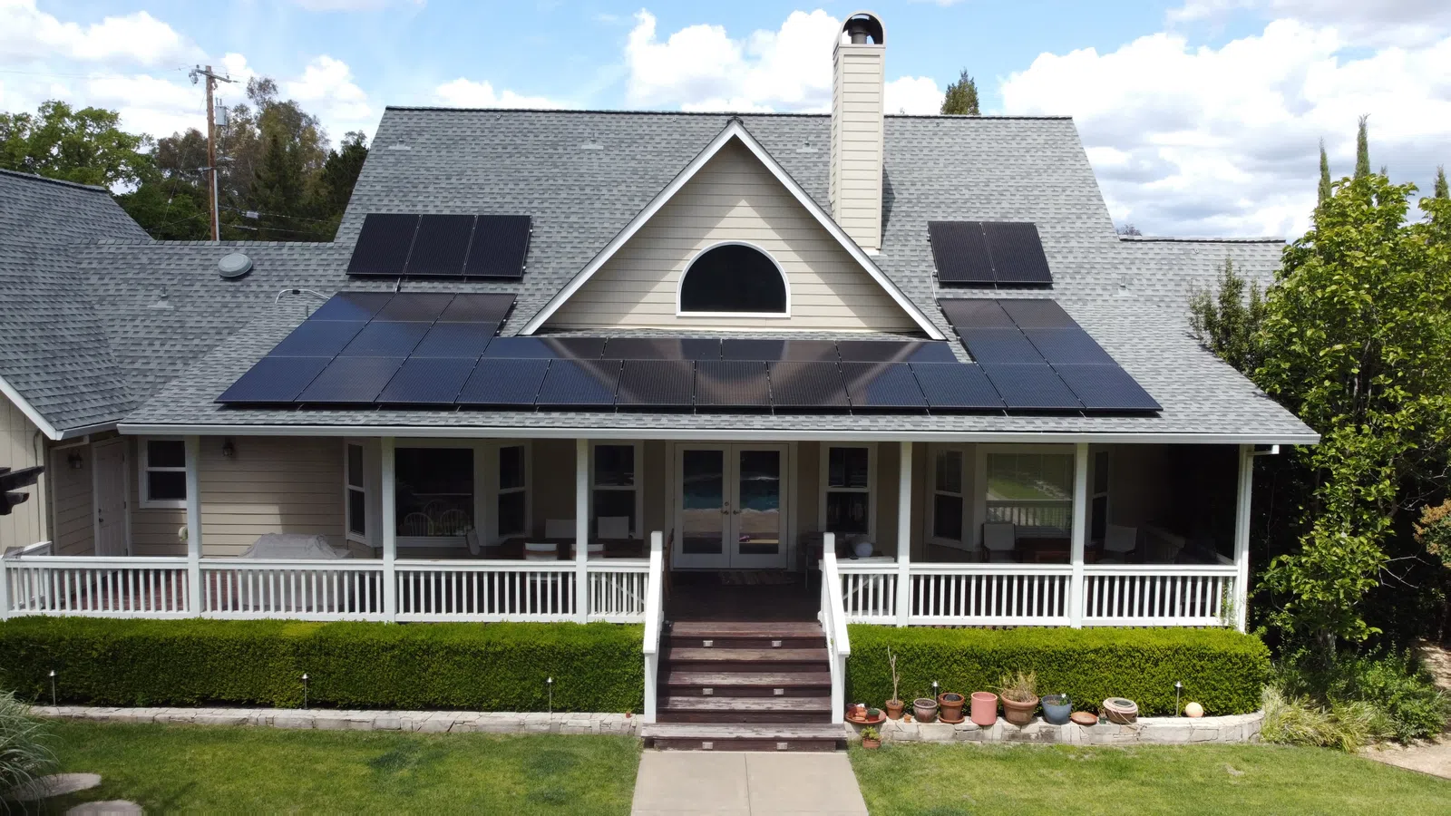 Suburban house with a gray roof featuring solar panels on a sunny day with a green lawn and blue sky.