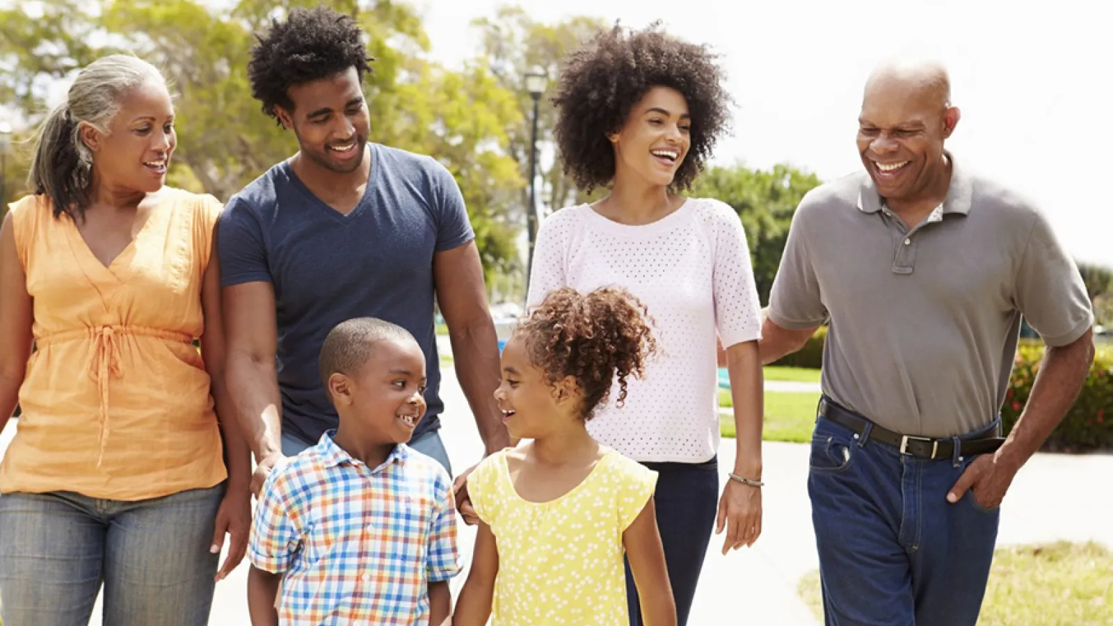 Happy multigenerational family walking outdoors smiling and enjoying time together in a sunny park.