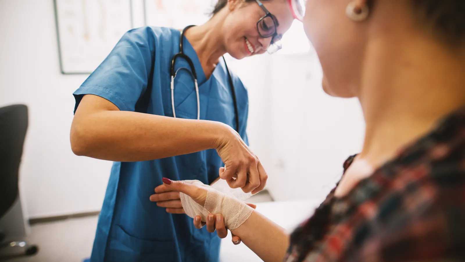 Healthcare professional wrapping a bandage on a patient's hand in a medical clinic with a smile