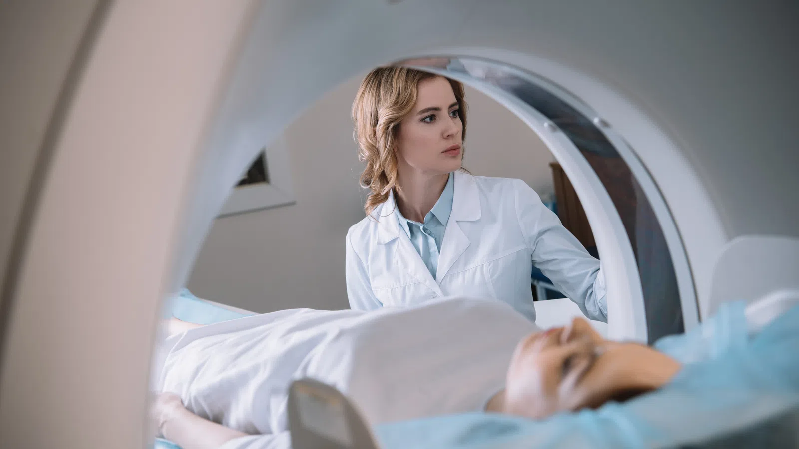 Medical professional operating MRI scanner as patient lies inside the machine for a brain scan.