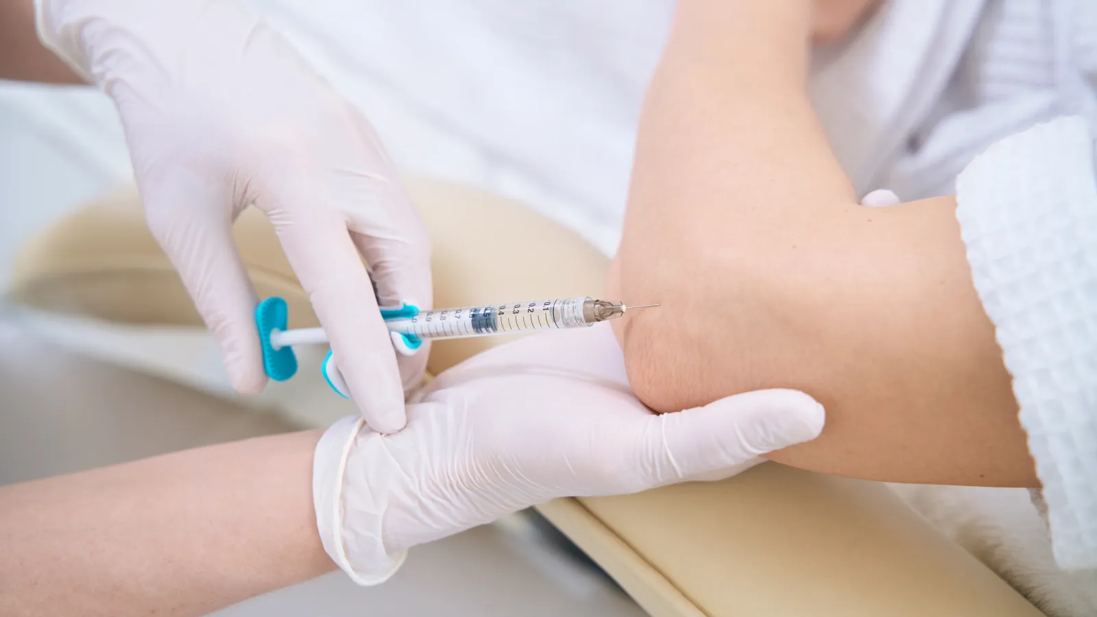 Medical professional wearing gloves injecting a syringe into a patient's elbow for treatment or vaccination.