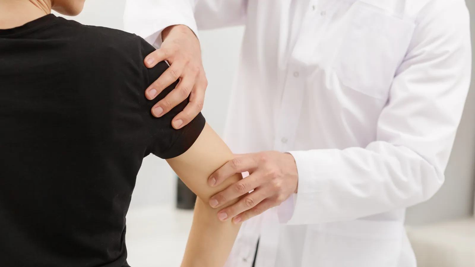 Doctor in white coat examining female patient's shoulder and arm for medical assessment.