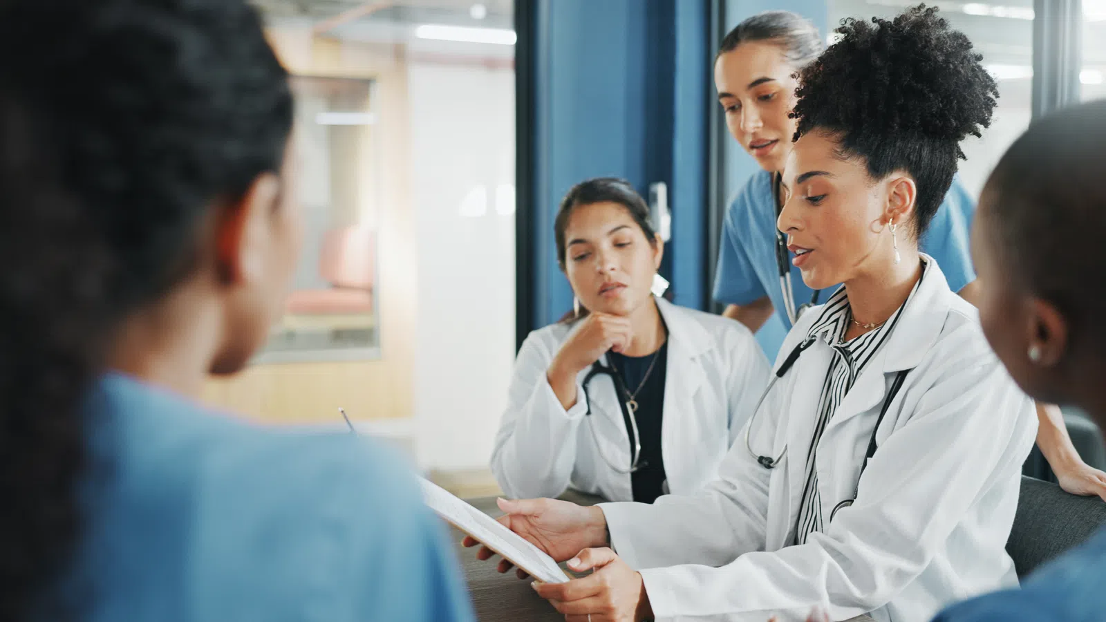 Female doctors and nurses discussing patient chart in a modern medical office meeting.