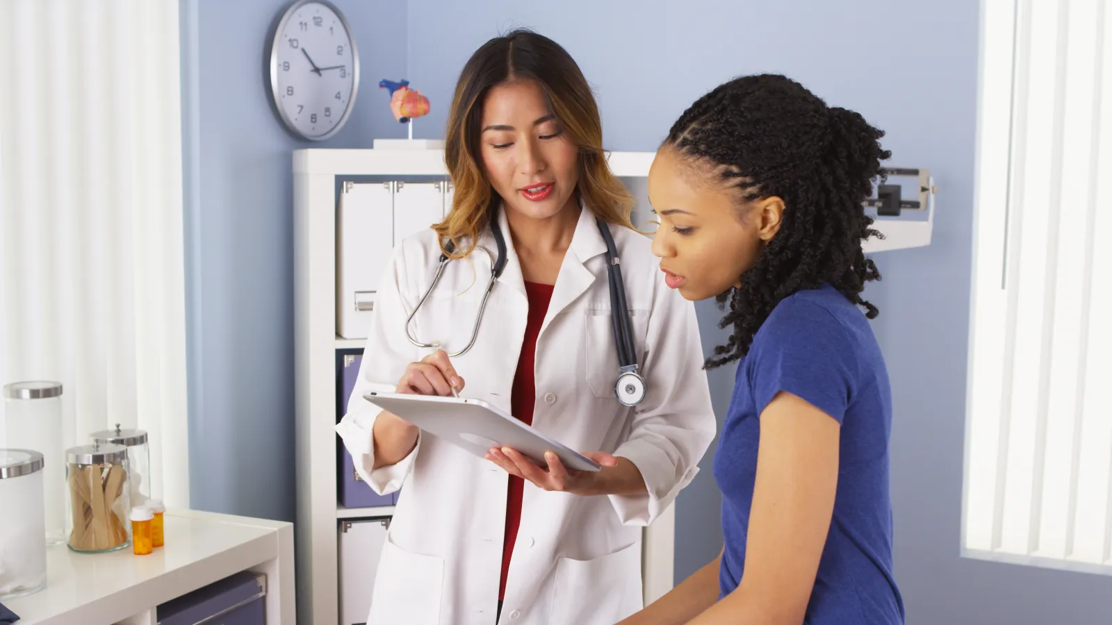Female doctor discussing medical information with young female patient in clinic setting.
