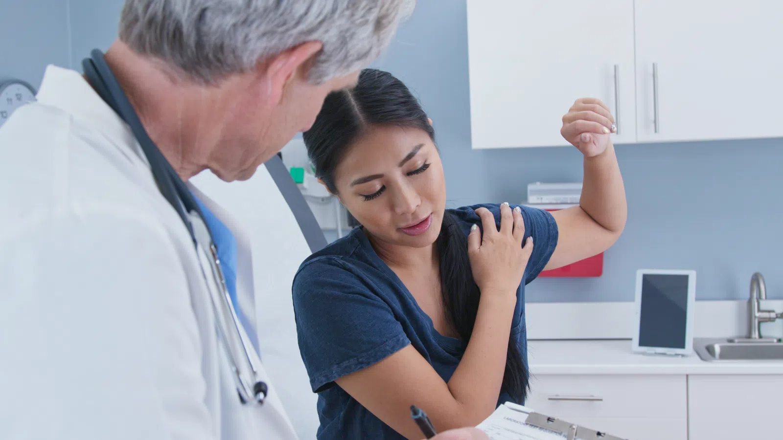 Doctor examining woman complaining of shoulder pain in a medical office during consultation.