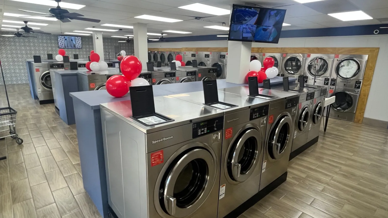 Modern laundromat with rows of stainless steel washers and dryers decorated with red and white balloons.