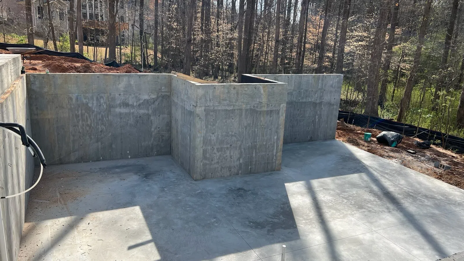 Concrete foundation walls and slab for a new house under construction in a wooded residential area.