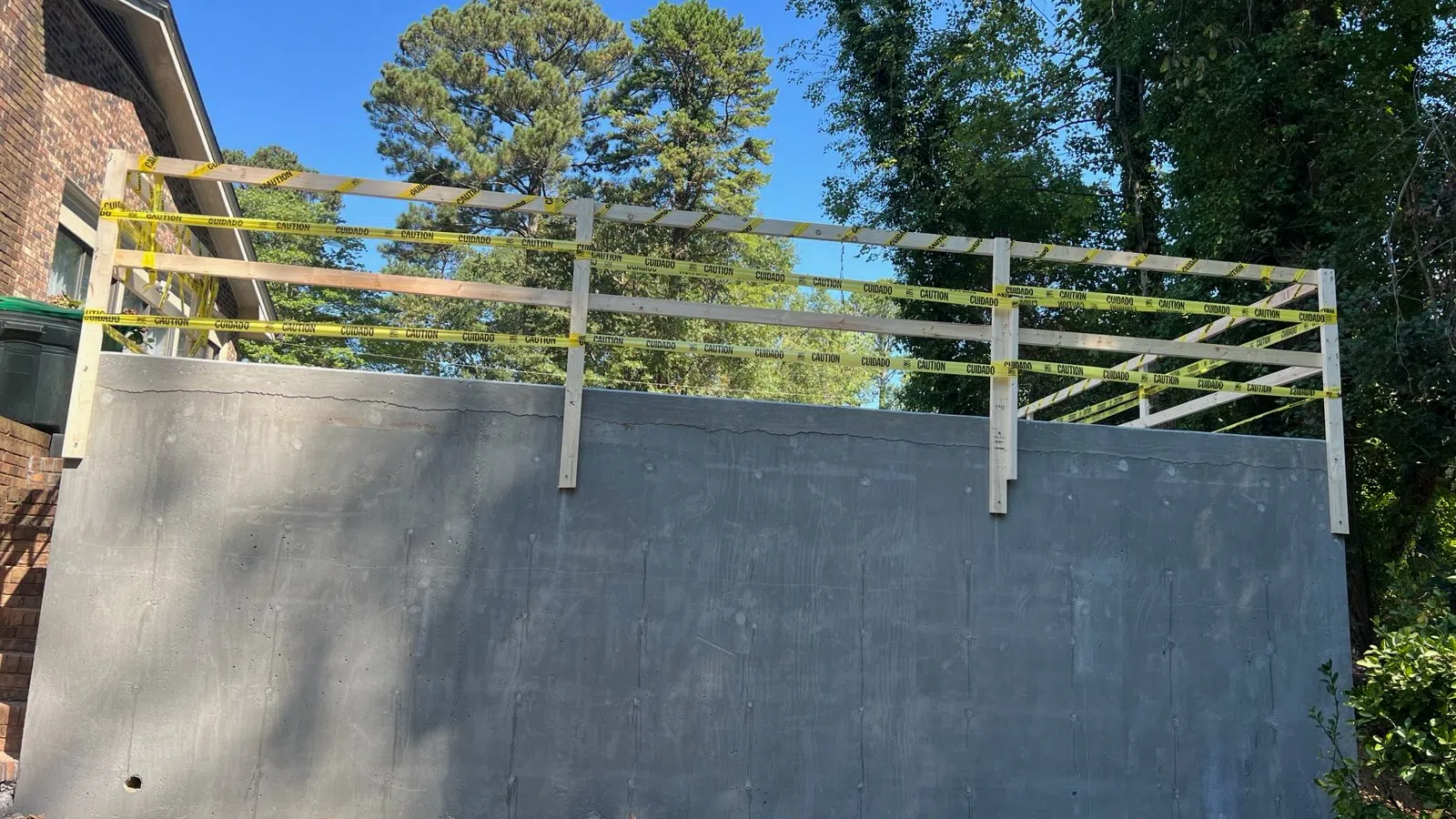 Newly built concrete retaining wall with wooden safety railings and caution tape on a sunny day