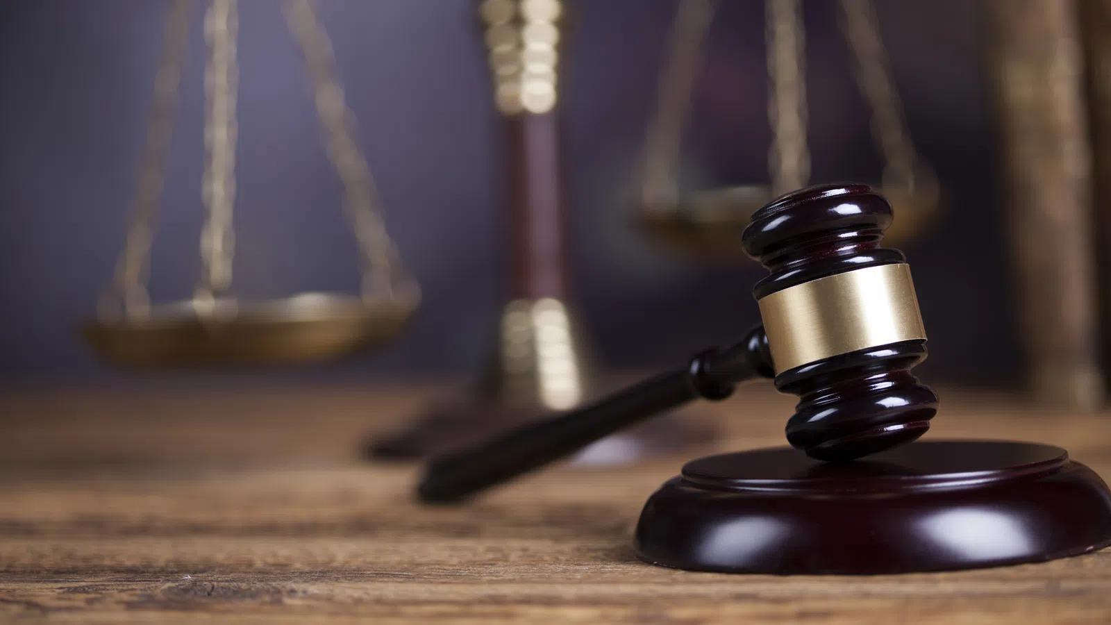 A wooden gavel resting on a desk, with scales of justice blurred in the background, symbolizing law and justice.