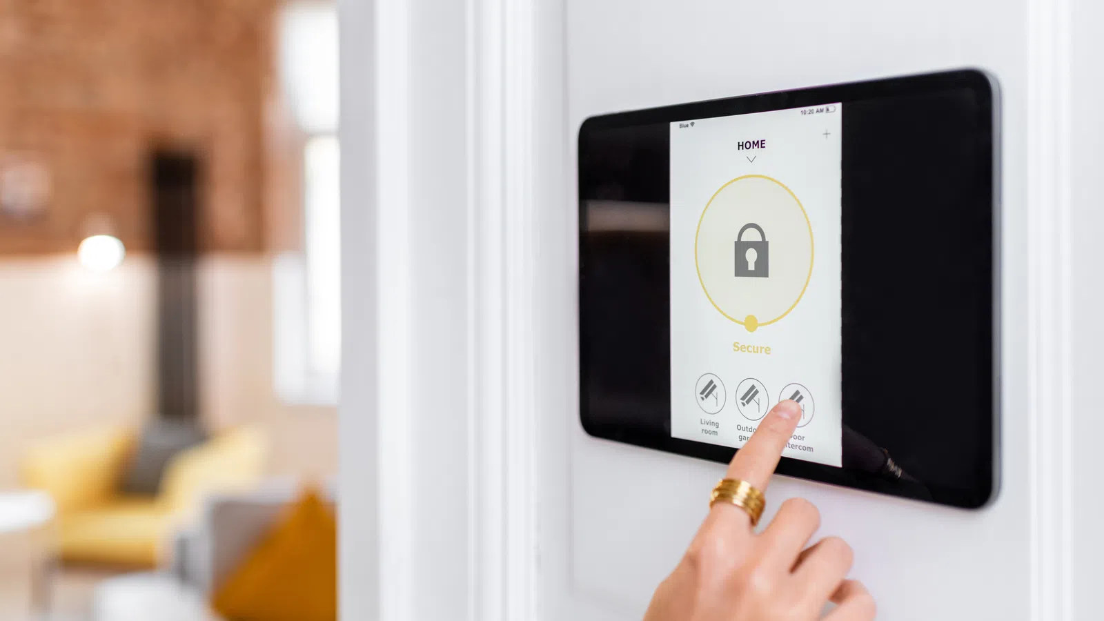 Person interacting with a home security touchscreen panel showing a locked icon and security status.
