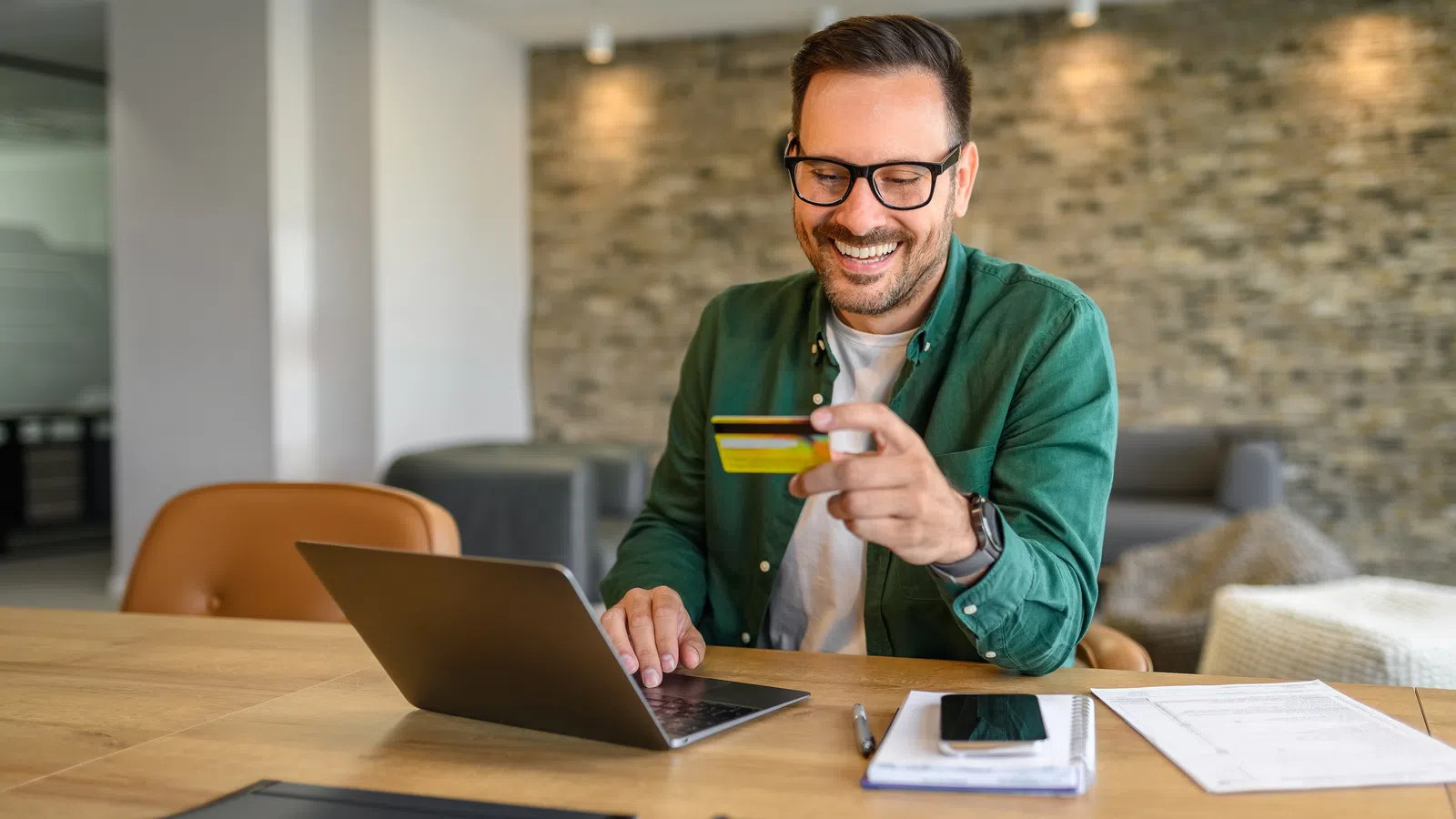 Man using laptop and credit card for online shopping or payment at home with documents on table