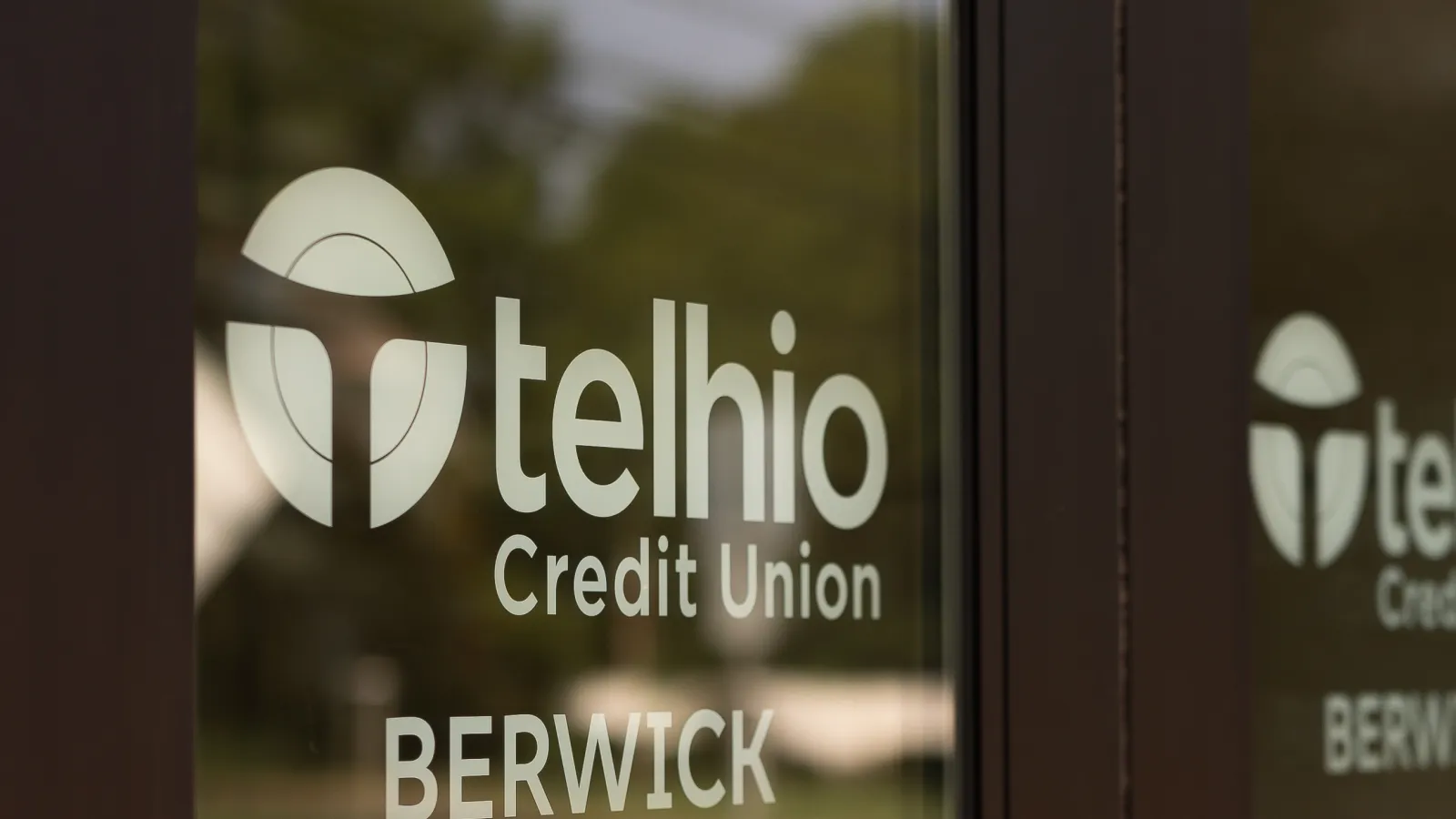 Glass door with Telhio Credit Union Berwick sign and logo reflecting outdoors on a sunny day.