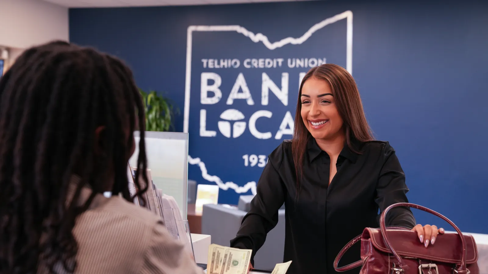 Smiling bank teller handing cash to customer at Telhio Credit Union with Bank Local sign in background