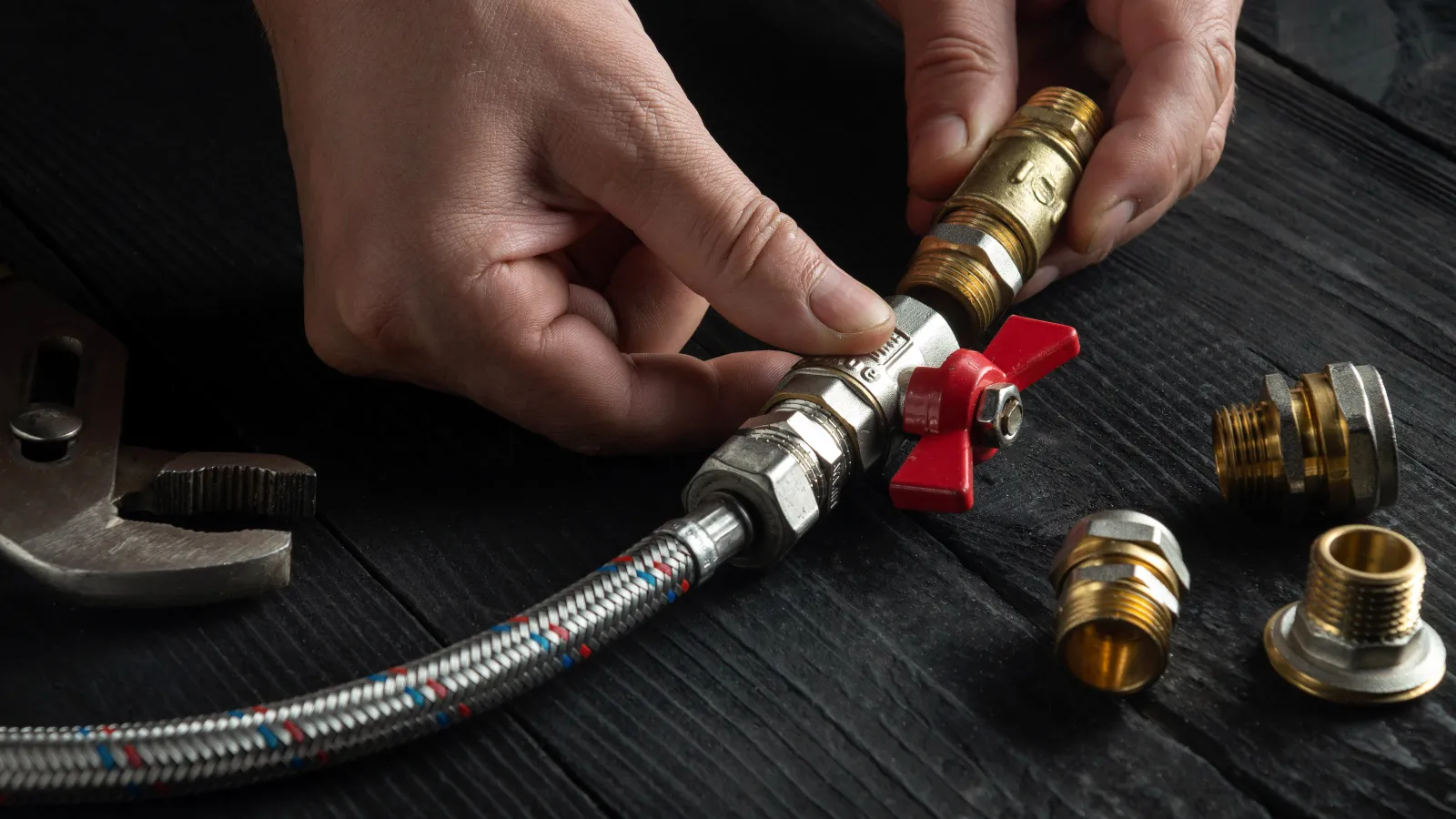 A person fixing plumbing with metal fittings and a wrench on a wooden surface.