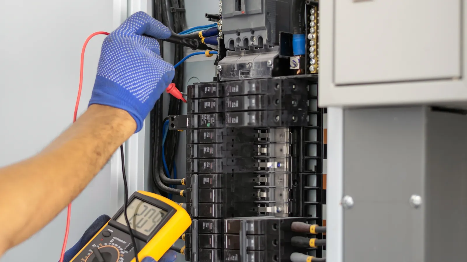 An electrician using a multimeter to check a circuit breaker panel.