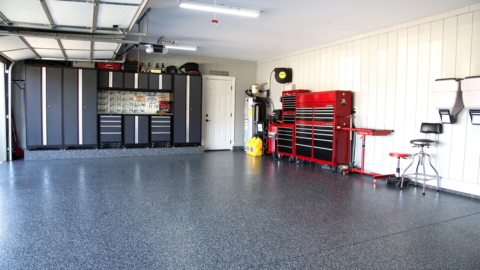 Clean and organized garage with black storage cabinets, red tool chests, and speckled epoxy flooring.