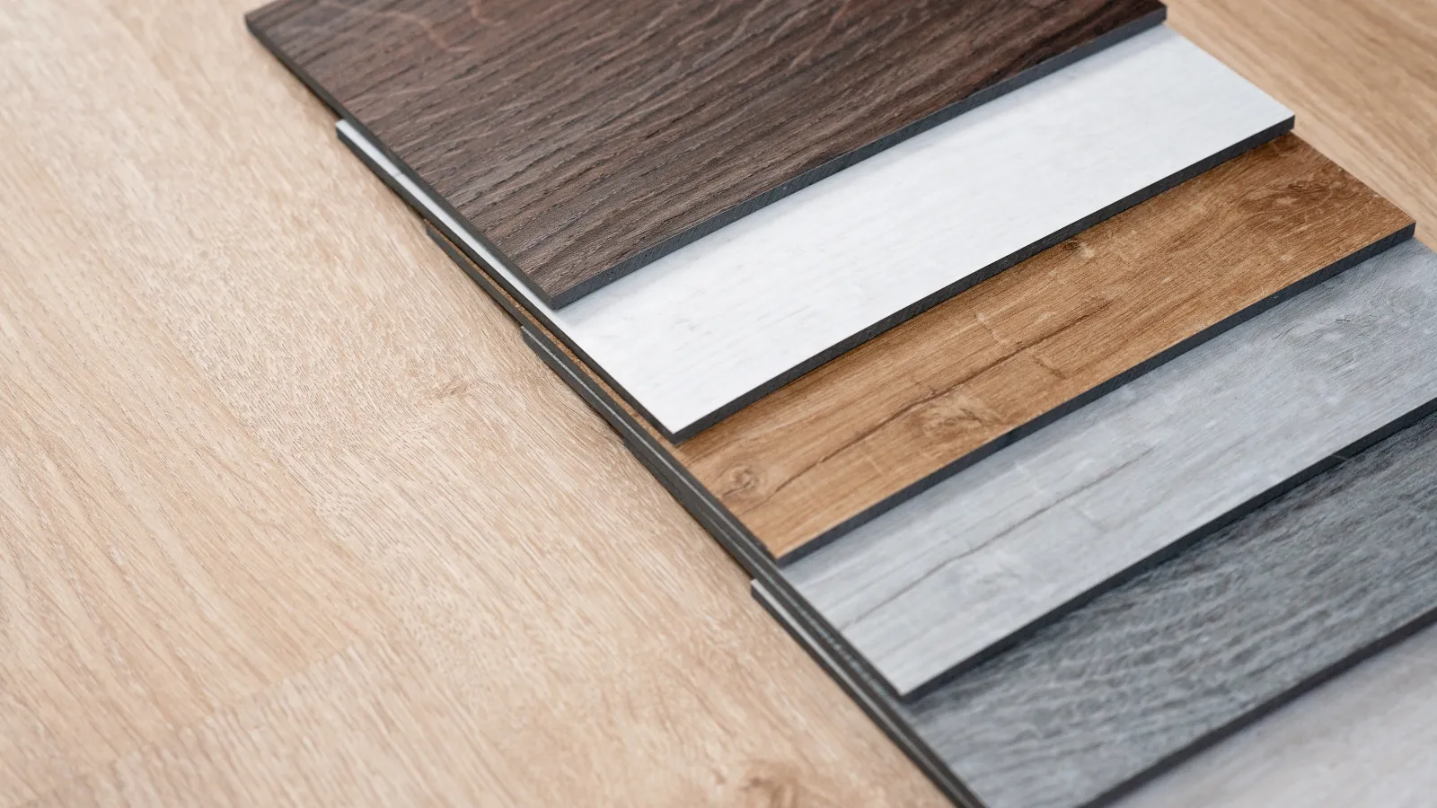 Samples of laminate flooring in various colors displayed on a light wooden surface.