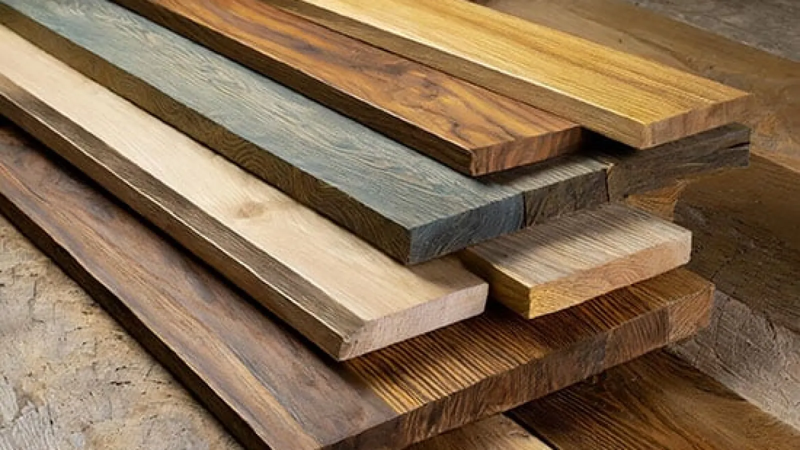 Stack of various wooden planks showcasing different colors, grains, and finishes on a wooden surface.