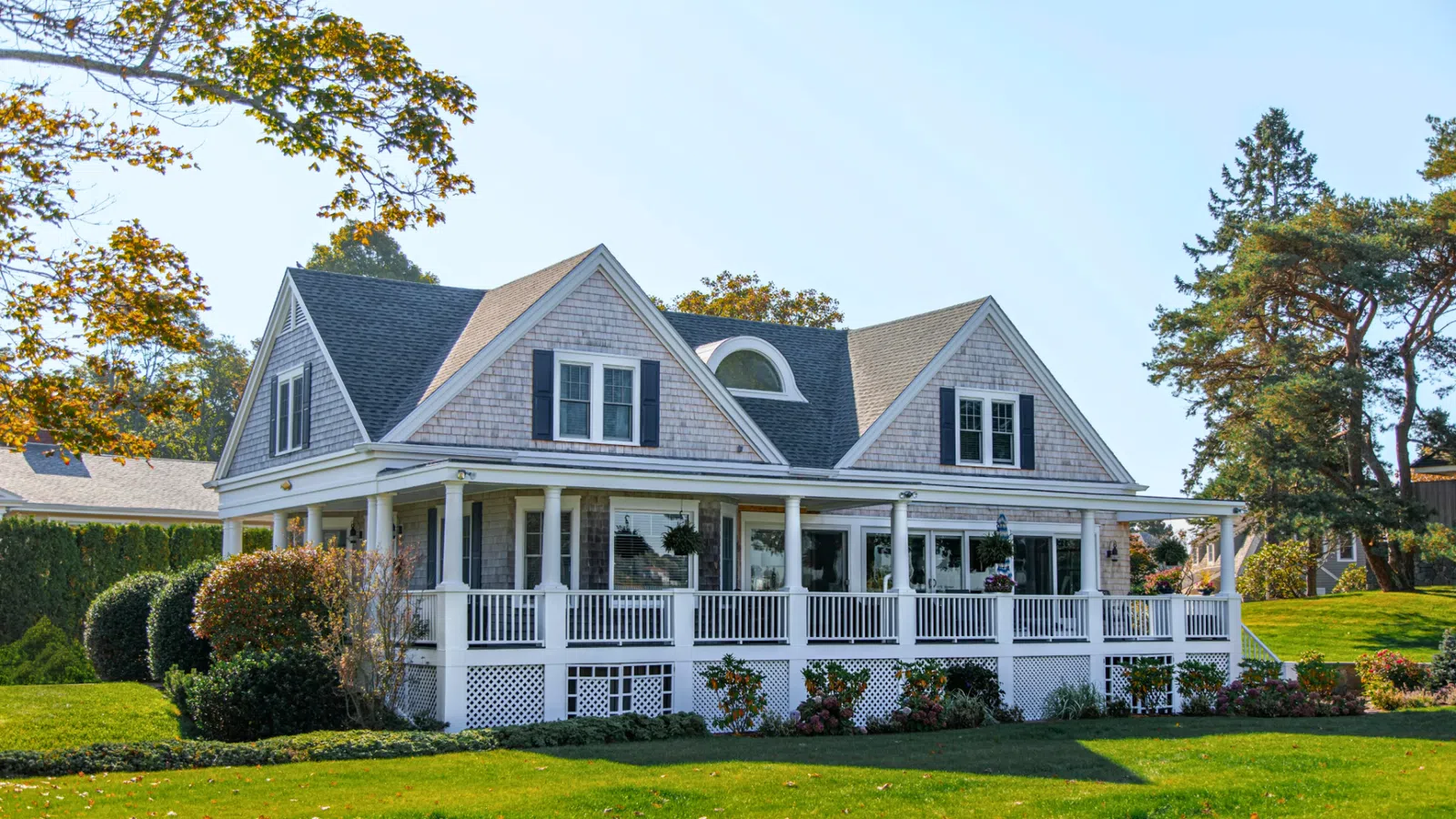 Cozy beach house with a spacious porch surrounded by greenery and trees, ideal for summer relaxation.
