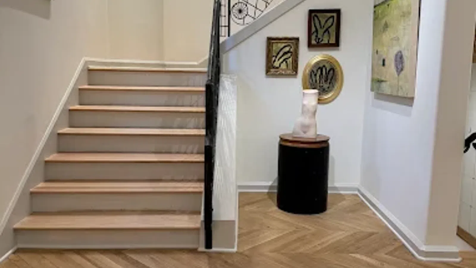 Modern staircase with light wood herringbone flooring, white walls, minimalist wall art, and decorative sculpture.