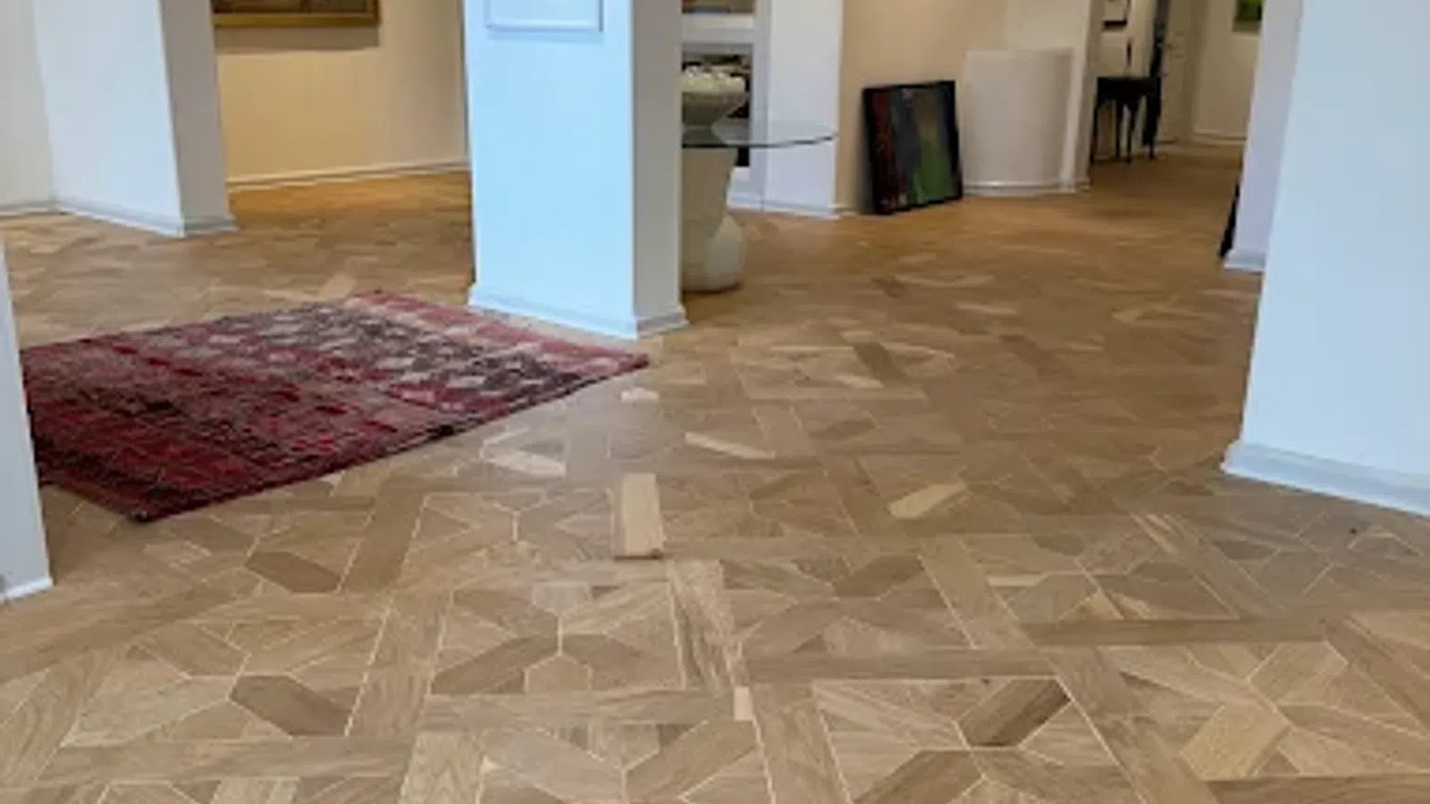 Intricate wooden parquet flooring in a bright art gallery with white walls and framed artwork.