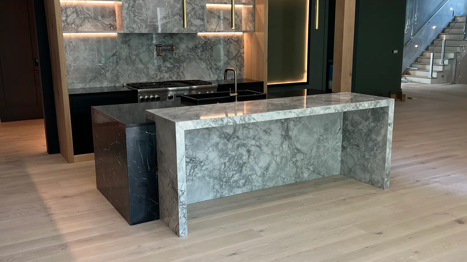 Modern kitchen with marble island and backsplash, wooden accents, pendant lights, and light hardwood flooring.
