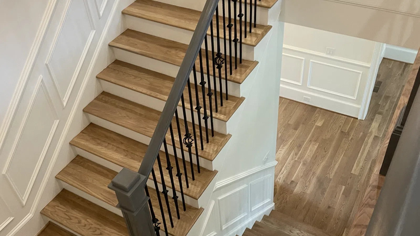 Interior view of wooden staircase with black metal balusters and white paneled walls in a modern home.