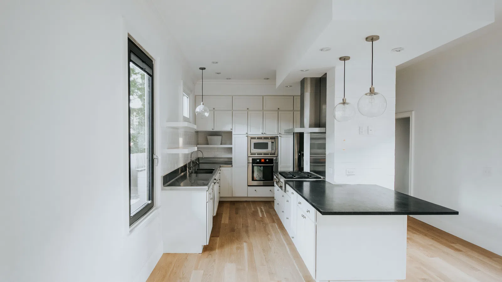 Bright modern kitchen with white cabinetry, black countertops, hardwood floors, and pendant lighting over island.