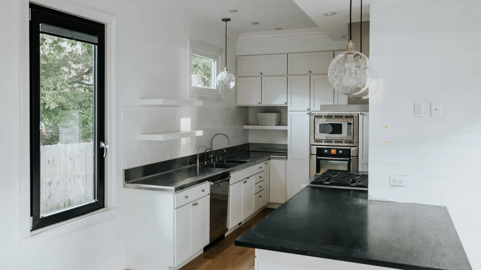 Bright modern kitchen with white cabinets, black countertops, wooden floor, and pendant lights over island.